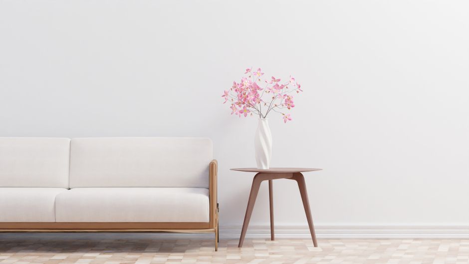 A modern minimalist living room featuring a white sofa and elegant floral decor on a wooden table.